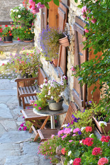 Fototapeta na wymiar colorful flowers potted and chairs in front of the facade pf an alpine house