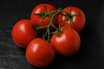 whole red tomatoes with green stems. on dark background. close up