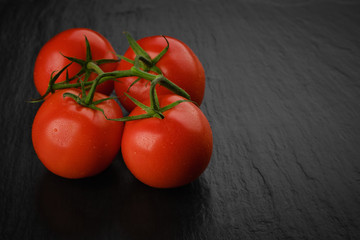 whole red tomatoes with green stems. on dark background. close up