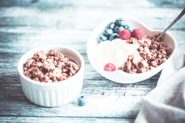 Greek yogurt, blueberries, raspberries and granola in a white bowl on a wooden background