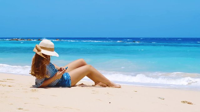 Young woman laying on sandy beach on smart phone Caribbean static shot