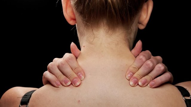 Woman doing self massage on her neck and shoulders. Black background.