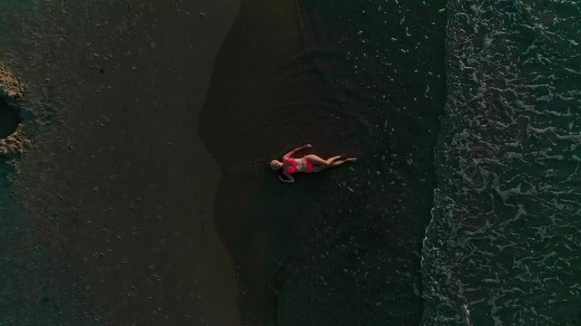 Aerial top view footage of a woman wearing bikini lying down on beach sand with waving sea water