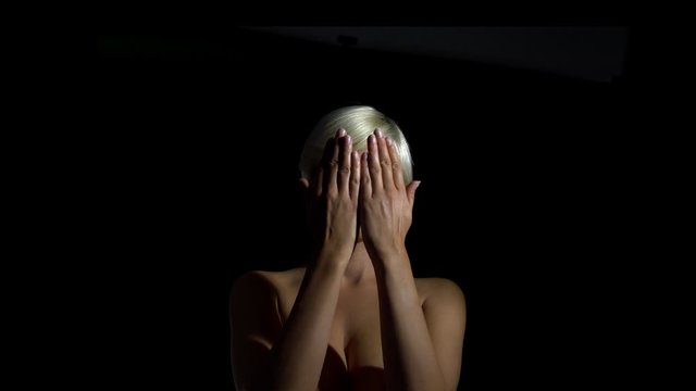 Close up portrait shot of short hair blonde woman covering her face with both hands on isolated black background