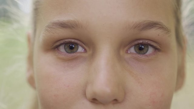 Extreme close-up of a young blond girl with hazel gray eyes looking at the camera. Pretty caucasian teen standing in the sunny park.