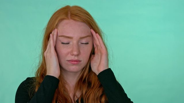 Woman in pain rubs her temples with hands, studio green screen.