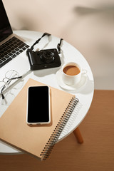 Office desk with mobile phone, coffee cup, laptop, camera and glasses