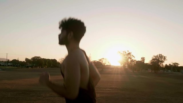 Indian guy running and trainning for cardio exercise on public park during sunset.