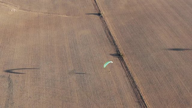 Nice aerial drone shot tracking paramotor having shadow while flying over the wide field