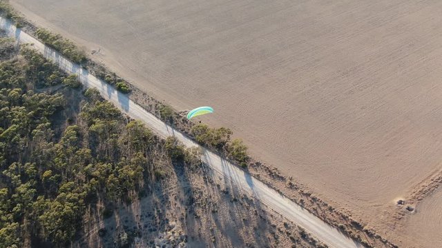 Aerial shot of powered paragliding flying over the long highway in countryside