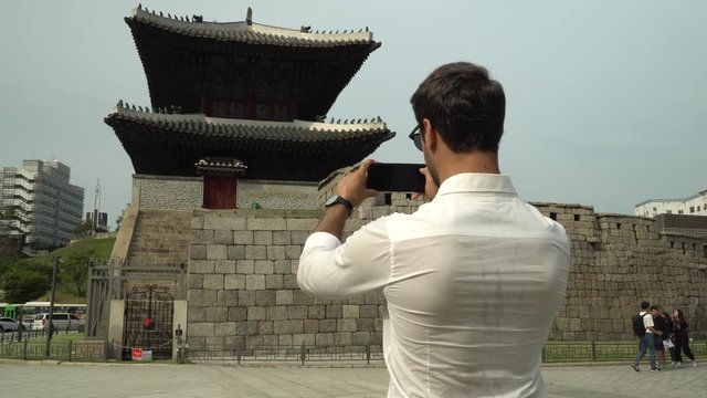 Male foreign visitor in Seoul Korea takes a picture of temple with his smart phone.