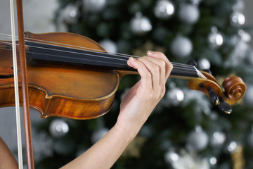 Hand of a female violinist on the fingerboard of a violin takes a chord with a decorated Christmas...