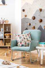Modern scandinavian interior design of childroom with mint armchair, climbing wall for kids, design furnitures, soft toys, teddy bear and cute children's accessories. Stylish kidroom decor. Template.