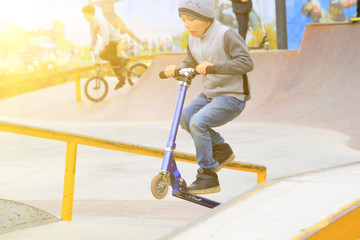 boy on kick scooter trains to ride and perform tricks like older guys in skate park