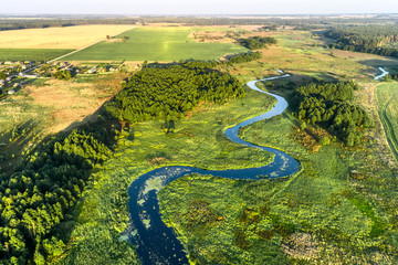 A small river flowing through meadows and agricultural fields. Aerial view. Evening shot with the...