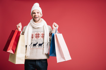 handsome smiling man in winter clothes holding shopping bags, isolated on red