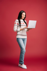 smiling woman in winter sweater using laptop isolated on red