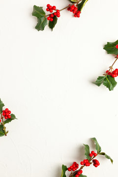 Christmas background with branches of holly with red berries on white. Winter concept. Flat lay, copy space.