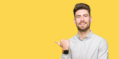 Young handsome man wearing casual shirt smiling with happy face looking and pointing to the side with thumb up.