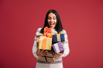 excited attractive woman holding christmas presents isolated on red