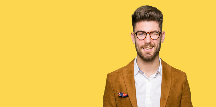 Young handsome business man wearing glasses winking looking at the camera with sexy expression, cheerful and happy face.