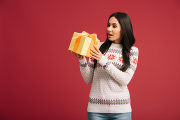beautiful shocked woman holding christmas present isolated on red