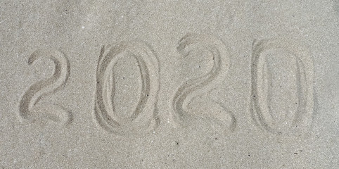 2020 written on dry white sea sand. Natural textured background. New year and Christmas travel concept. Design idea for greeting cards, postcards, invitations, promotion, websites
