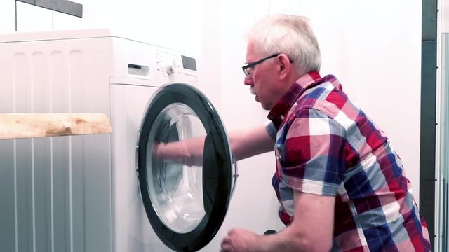 Senior man turning on washing machine in the bathroom