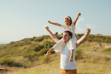 Fototapeta premium Father and daughet spending time together taking a walk in the green mountain fields on their vacation. Father holding the girl on his back.