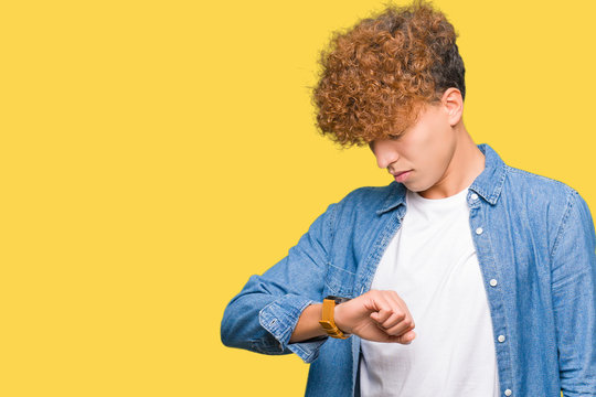 Young handsome man with afro hair wearing denim jacket Checking the time on wrist watch, relaxed and confident