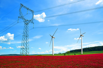 High voltage power lines with wind turbines in crimson clovers field. Renewable electric energy...