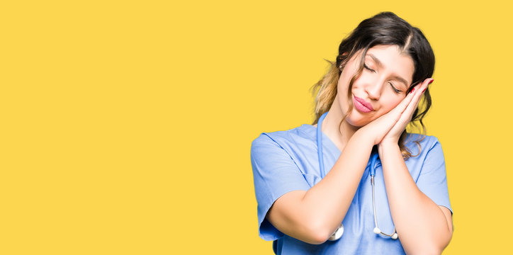 Young adult doctor woman wearing medical uniform sleeping tired dreaming and posing with hands together while smiling with closed eyes.