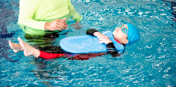 One girl wearing a swimsuit uses a foam pad to practice swimming in a swimming pool with a teacher. She happily and smiling.