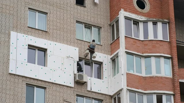 Climbers are working on the insulation of facades of a multi-storey residential building. Builder working at height while holding on a rope and insurance