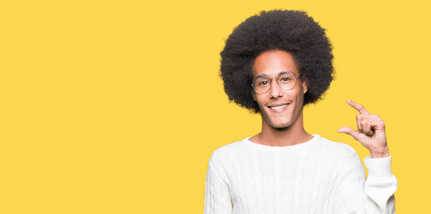 Young african american man with afro hair wearing glasses smiling and confident gesturing with hand doing size sign with fingers while looking and the camera. Measure concept.