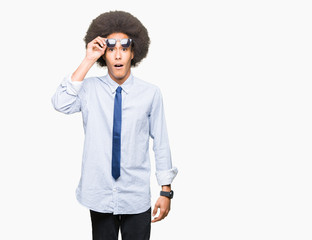 Young african american business man with afro hair wearing sunglasses afraid and shocked with surprise expression, fear and excited face.