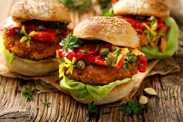 Pumpkin burgers with the addition of grilled peppers, fresh lettuce, herbs and capers on a wooden rustic background, close-up. Vegan burgers