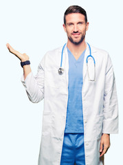 Handsome doctor man wearing medical uniform over isolated background smiling cheerful presenting and pointing with palm of hand looking at the camera.