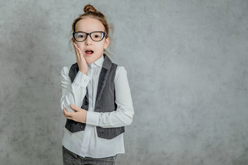 Portrait of a beautiful little girl standing on a gray background. During this surprised look.