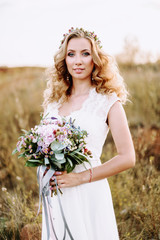 Portrait of a bride in a beautiful dress with a wedding bouquet in her hands. In a beautiful wheat field at sunset