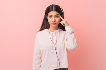 Young arab woman listening to music pointing his temple with finger, thinking, focused on a task.