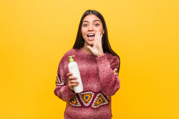 Young arab woman holding a cream bottle shouting excited to front.