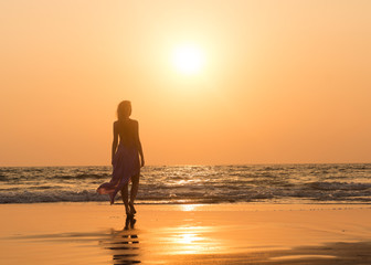 Fototapeta na wymiar Girl wearing maxi skirt walking on the beach at sunset. Lady's silhouette