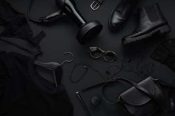 Black monochromatic flatlay on black background. Clothes, accessories and beauty equipment. Black...