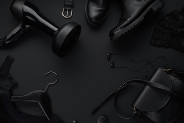 Black monochromatic flatlay on black background. Clothes, accessories and beauty equipment. Black...