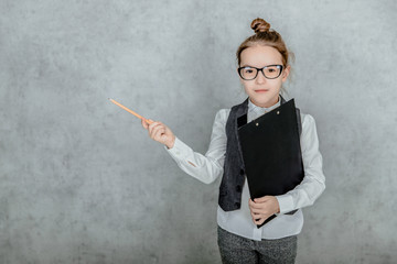 The little lady boss is on a gray background. During this, he holds a black folder and raised the yellow pencil to the side looking at the camera.
