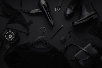 Black monochromatic flatlay on black background. Clothes, accessories and beauty equipment. Black friday sale concept