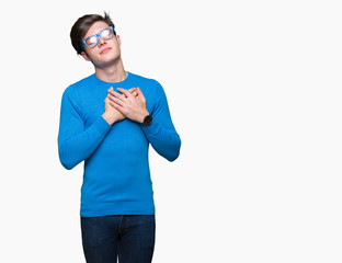 Young handsome man wearing blue glasses over isolated background smiling with hands on chest with closed eyes and grateful gesture on face. Health concept.