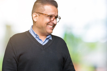 Middle age bussines arab man wearing glasses over isolated background looking away to side with smile on face, natural expression. Laughing confident.