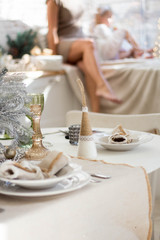 Beautiful served table with decorations, candles with glaze on white tablecloth on the background of the kitchen with people. Living room d